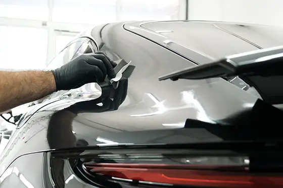 Die Mitarbeiter tragen bei der Arbeit Chemikalienschutzkleidung. Automobilindustrie. Autowasch- und Beschichtungsbetrieb mit Keramikbeschichtung. Aufsprühen des Lacks auf das Auto. Konzept: Fahrzeugschutz, Service, Glanz.